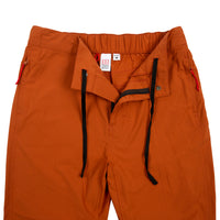 General front detail shot of Topo Designs Women's Lightweight Tech Pants in Brick orange showing zipper fly opening and drawstring at waist.