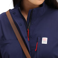 General detail shot of zipper, snaps, and chest zipper pocket & logo on model wearing Topo Designs Women's Coverall jumpsuit in "Navy" blue. 