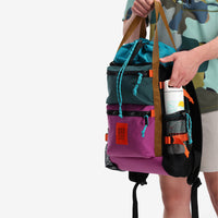General shot of model holding pack, showing water bottle holder feature of the Topo Designs River Bag cinch top tote backpack with mesh sides in "Botanic Green / Grape" green recycled nylon.